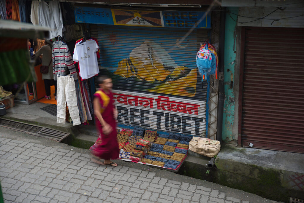 Young monk passing a Free Tibet shop shutter, Dharamshala and McLeod Ganj