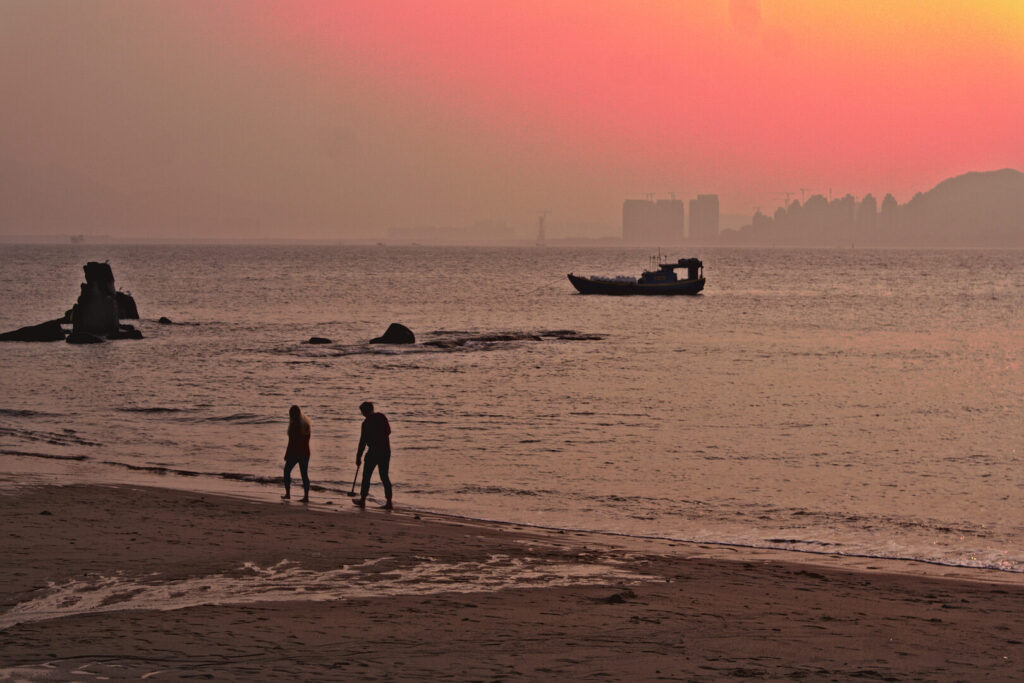 Two figures at the water's edge, dusk, Xiamen in January